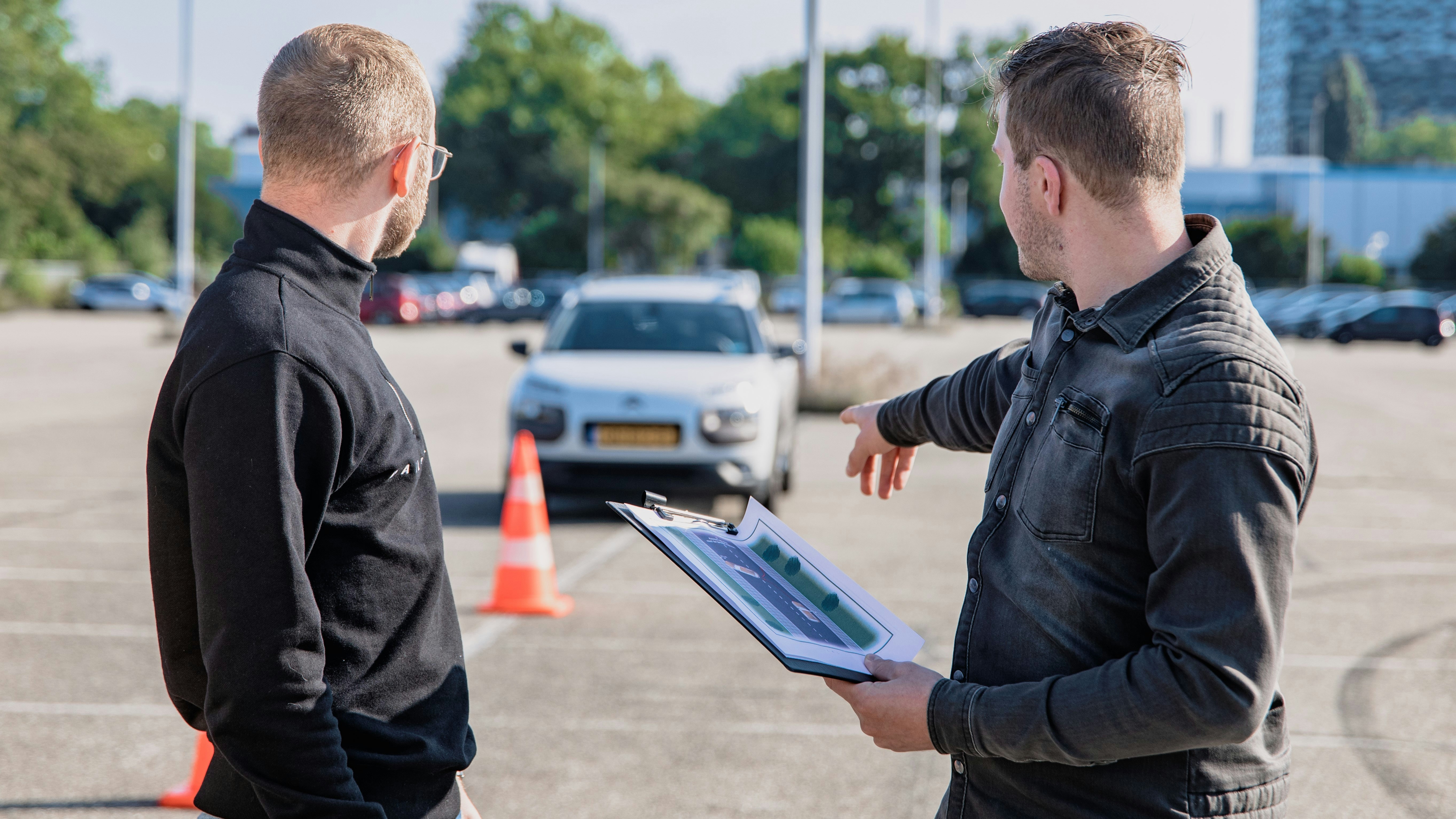 Driving instructor pointing at a car during a test in a parking lot marked with cones