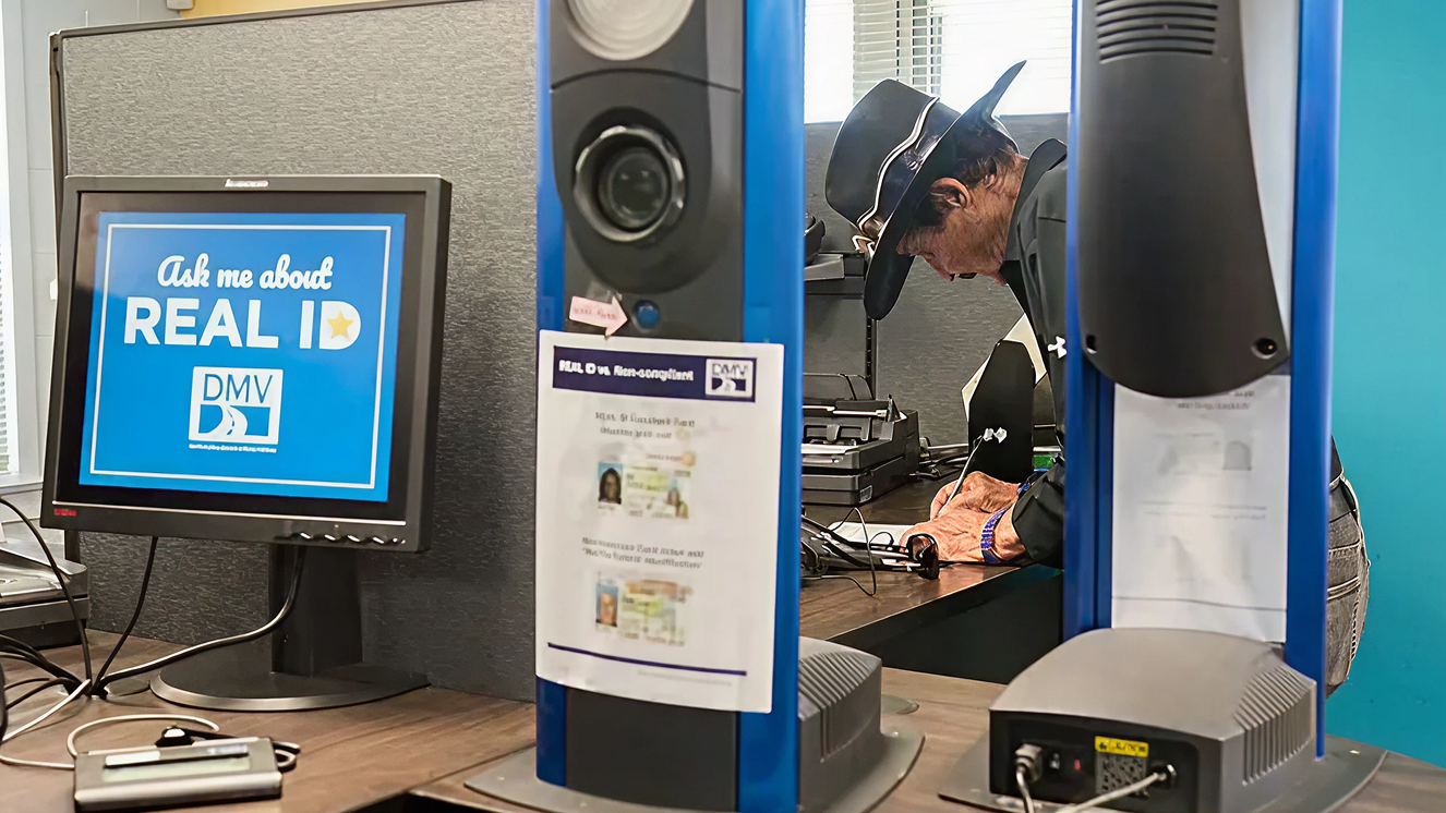 モニターに「REAL ID」の案内が表示されたDMVオフィス内で、カウンターに身をかがめる男性
