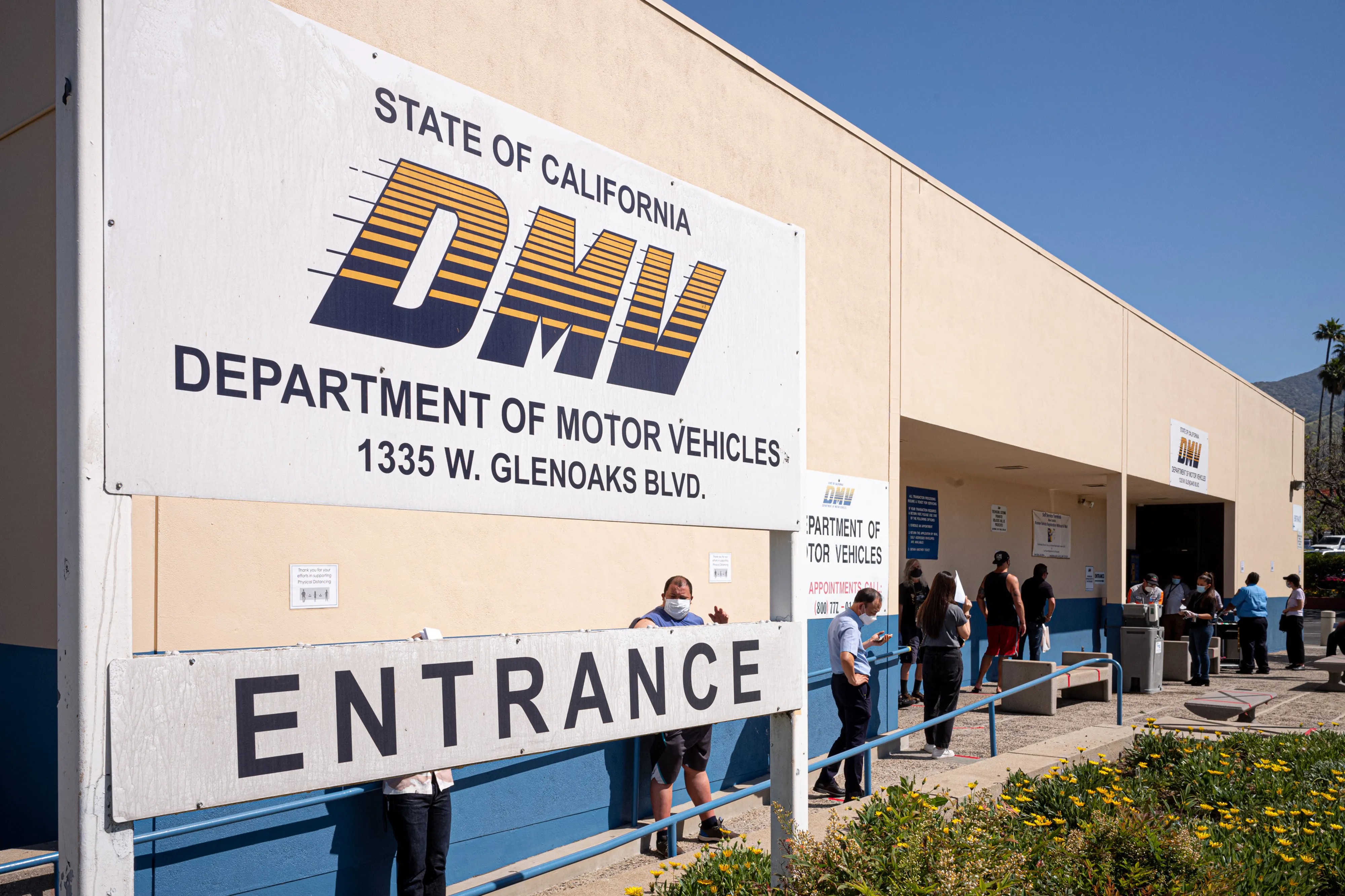 「DMV」の看板とENTRANCE(入口)表示があるカリフォルニアDMVオフィスの外観、外で待つ人々
